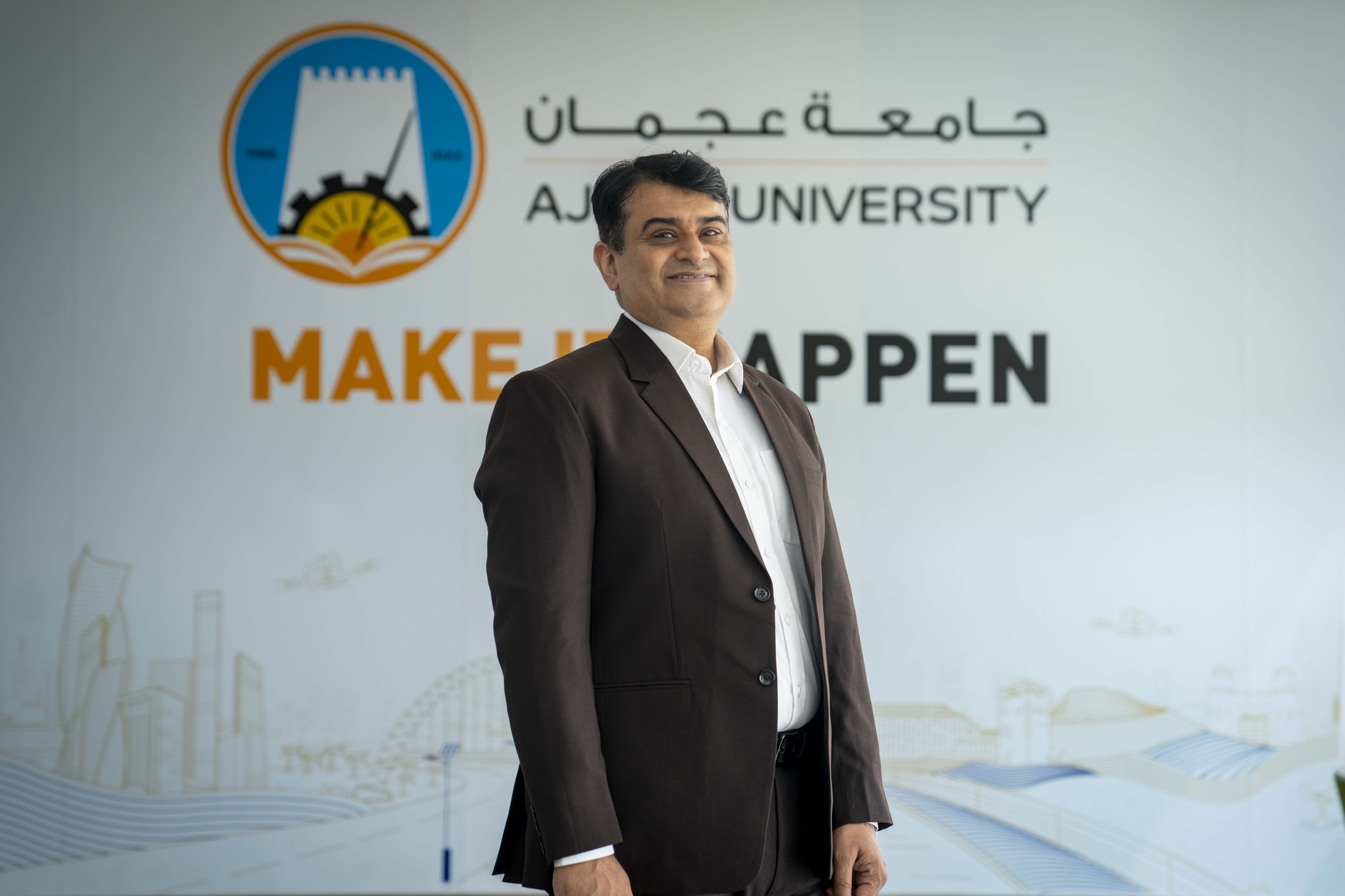 Man in suit at Ajman University backdrop.